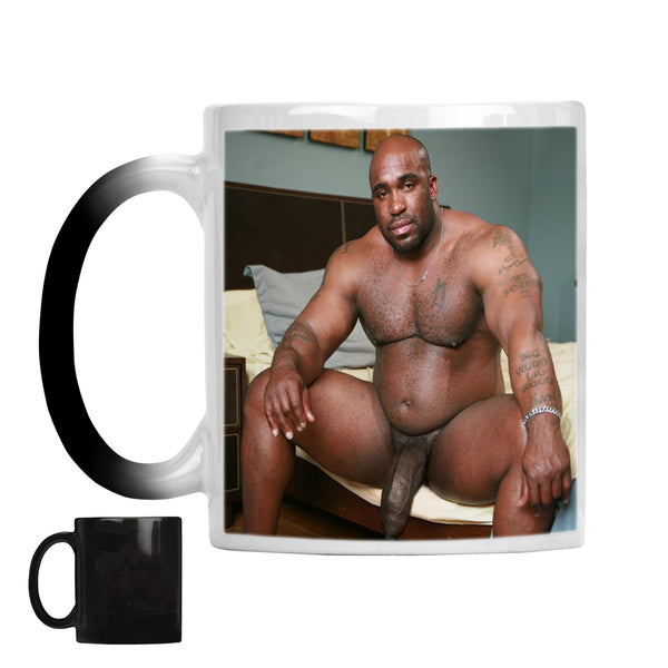 A white ceramic mug with a black-to-white gradient handle, featuring a printed photo of a shirtless tattooed NAKED man sitting on a bed. A smaller inset shows the mug turned black, indicating a color-changing or alternate view design.