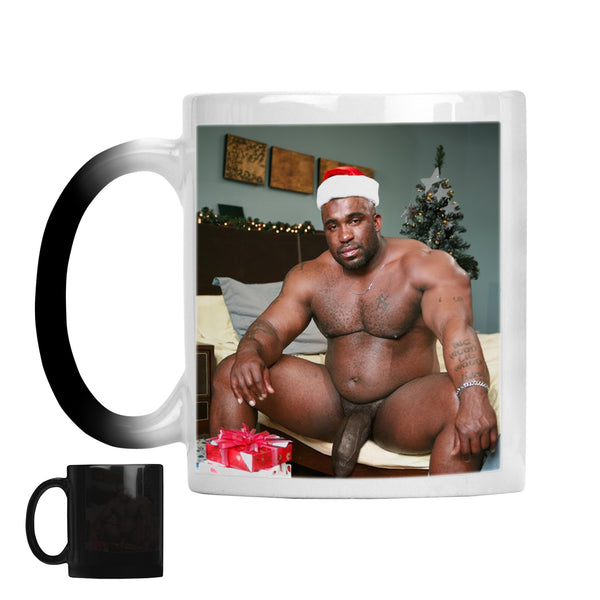 A ceramic mug with a black-to-white colour-changing handle and body, shown alongside its fully revealed state. The revealed mug features a printed photo of a shirtless naked man wearing a Santa hat in a bedroom with a Christmas tree and wrapped gifts.