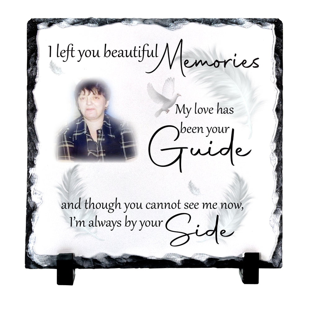 Personalized memorial slate plaque with a photo of a deceased loved one, white feathers, and black text reading 'I left you beautiful Memories My love has been your Guide and though you cannot see me now, I'm always by your Side', displayed on a black stand against a white background.