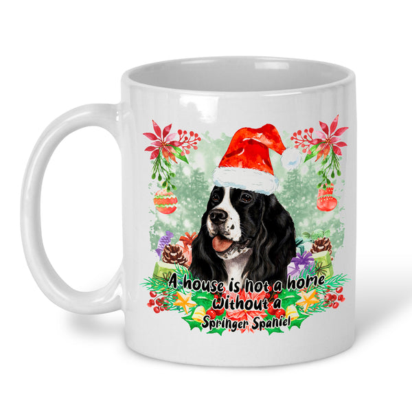 A white ceramic mug featuring a festive Christmas design with a Springer Spaniel dog wearing a Santa hat, surrounded by poinsettias, ornaments, pinecones, and the text 'A-house is not a home Without a Springer Spaniel'.