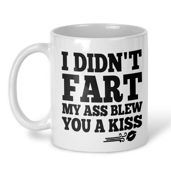 A white ceramic coffee mug with bold black text that reads 'I DIDN'T FART MY ASS BLEW YOU A KISS' and a small kiss mark graphic, shown on a clean white background.
