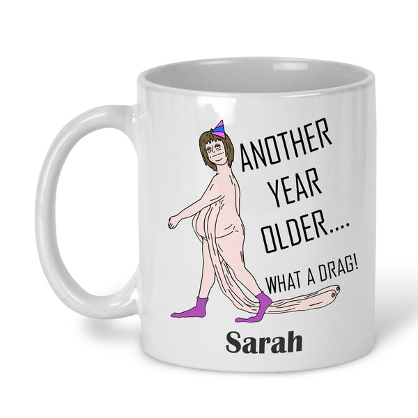 A white ceramic mug with a printed cartoon character and the text 'ANOTHER YEAR OLDER' personalised with name
