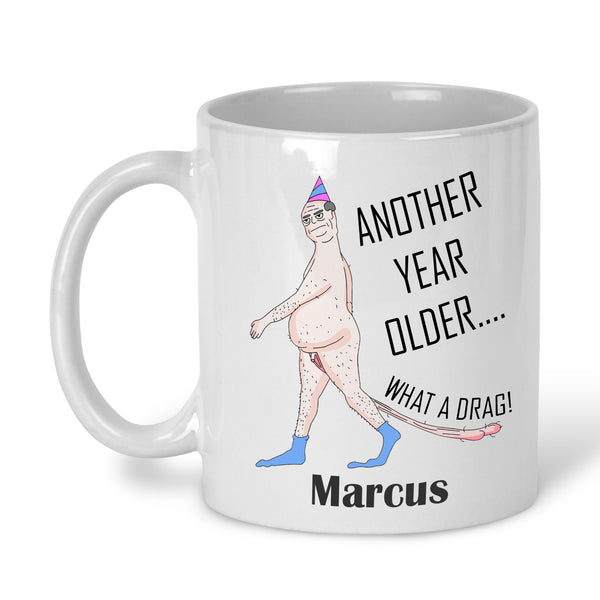 A white ceramic mug with a printed cartoon character and the text 'ANOTHER YEAR OLDER' personalised with name